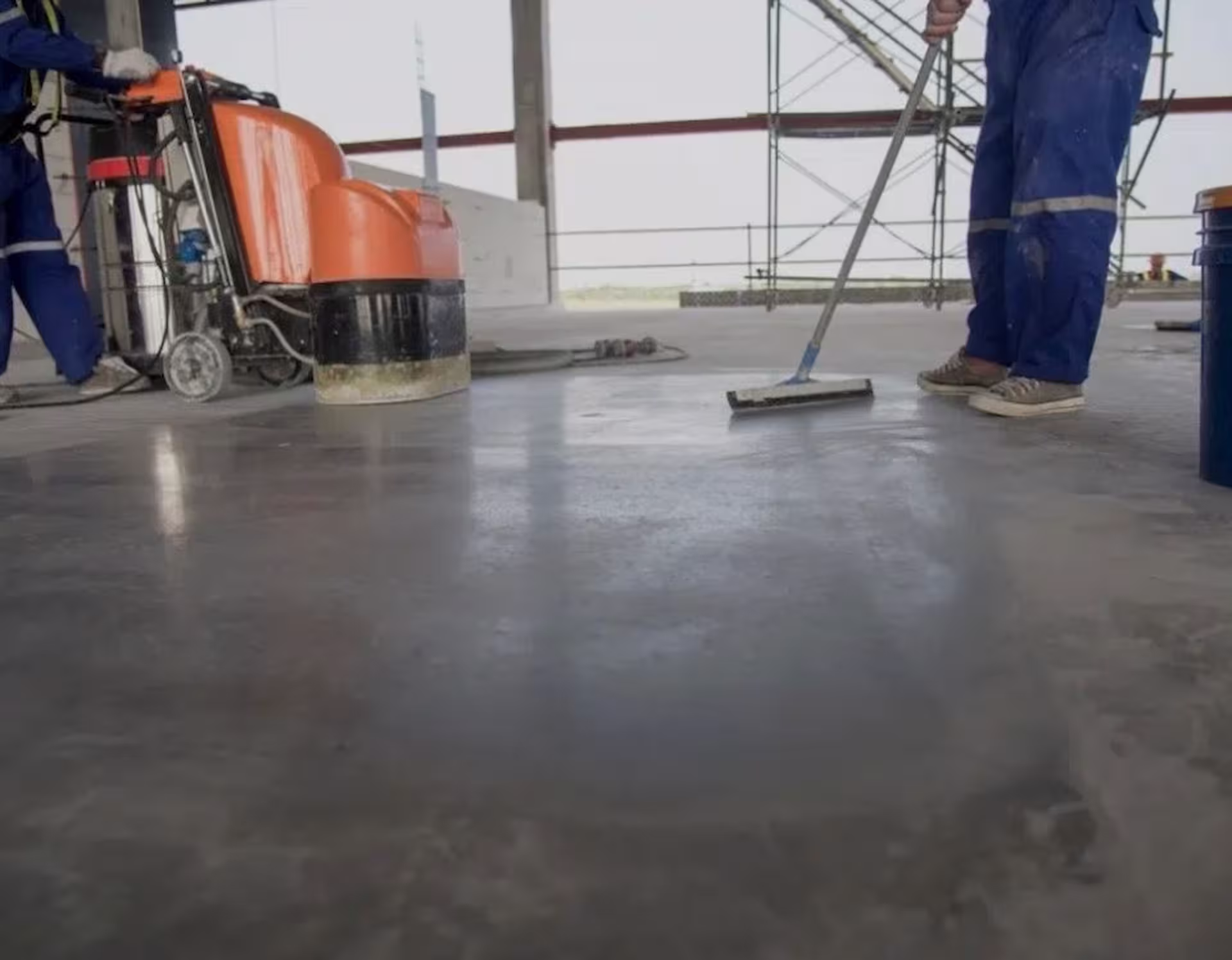 Arbetare som rengör och polerar ett stort betonggolv i en industrilokal med golvmaskin